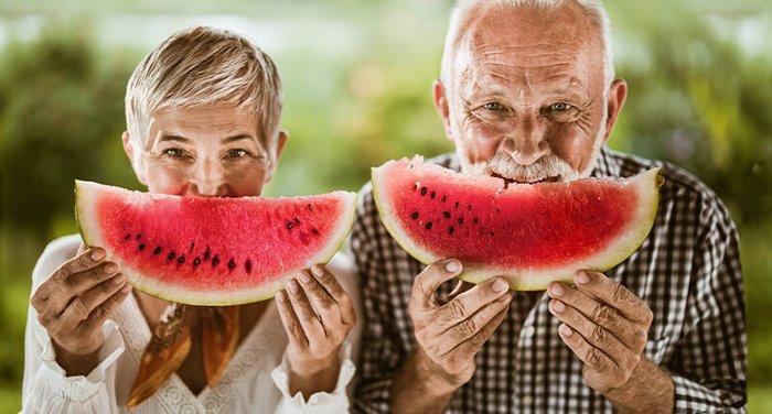Älterer Mann und Frau halten Wassermelonen vor Gesichter