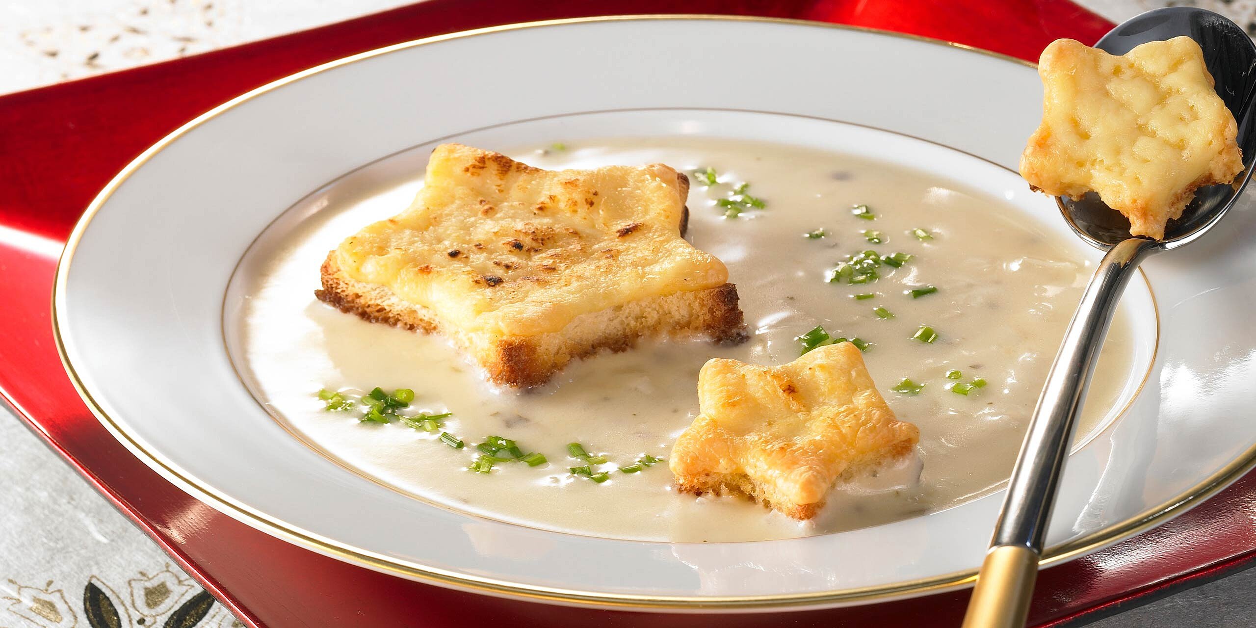 Cremige Suppe mit goldbraunen Käsetoast-Sternen auf weißem Teller.