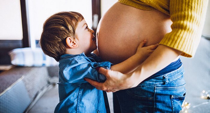 Kleiner Junge küsst schwangere Mutter auf den Bauch