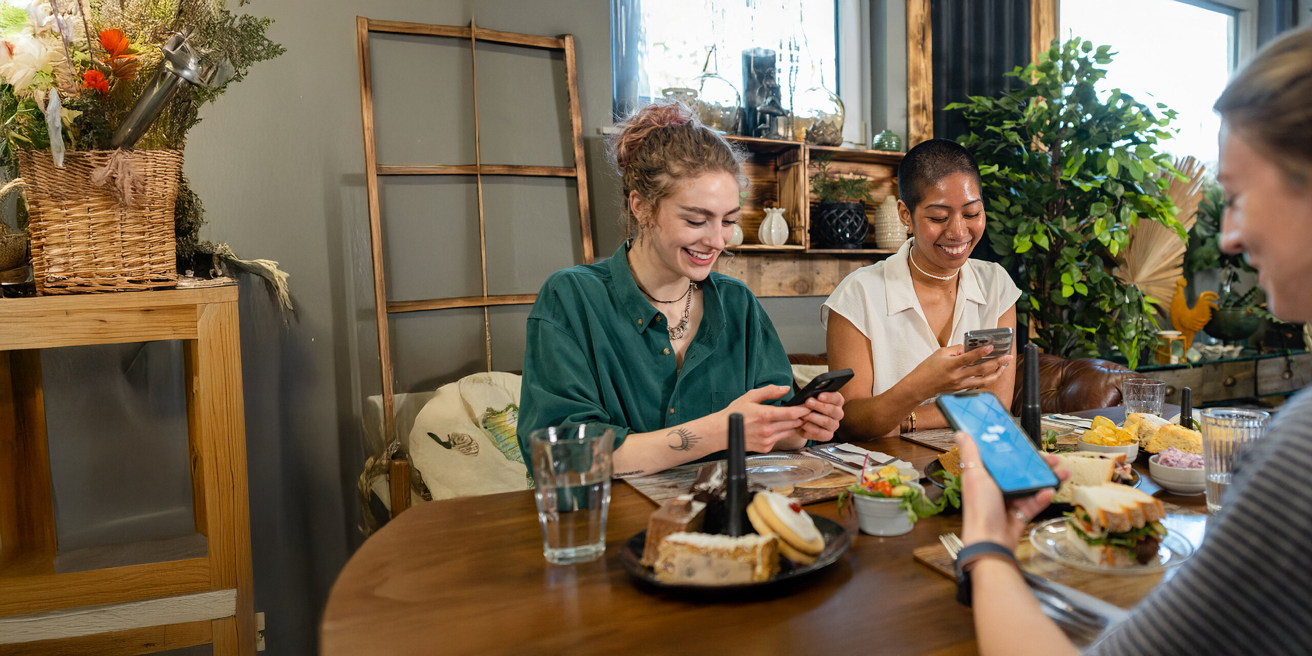 Freundinnen genießen ein Essen und teilen etwas auf ihren Smartphones.