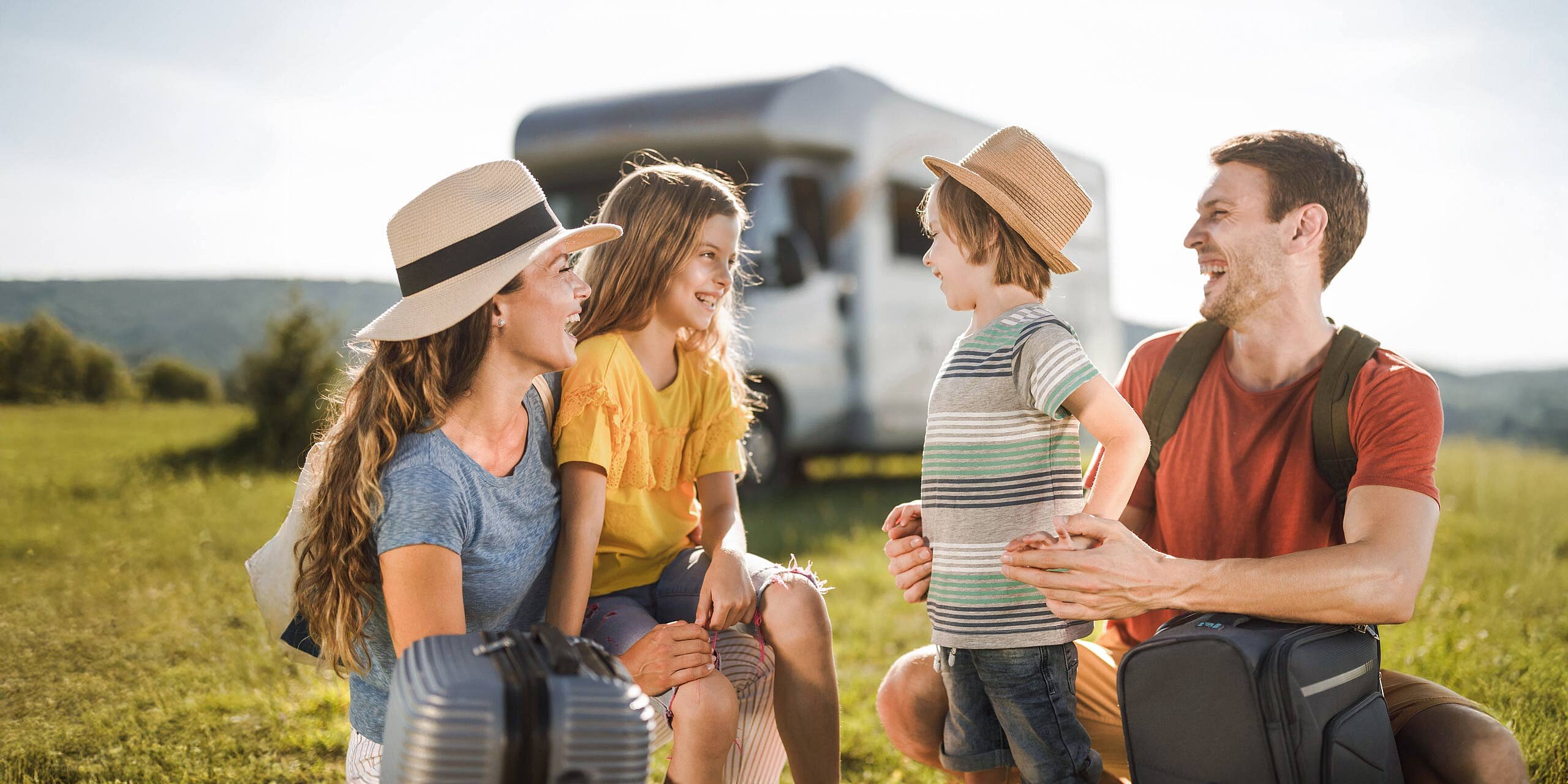 Familie mit zwei Kindern vor Wohnmobil lacht und genießt Urlaub in der Natur