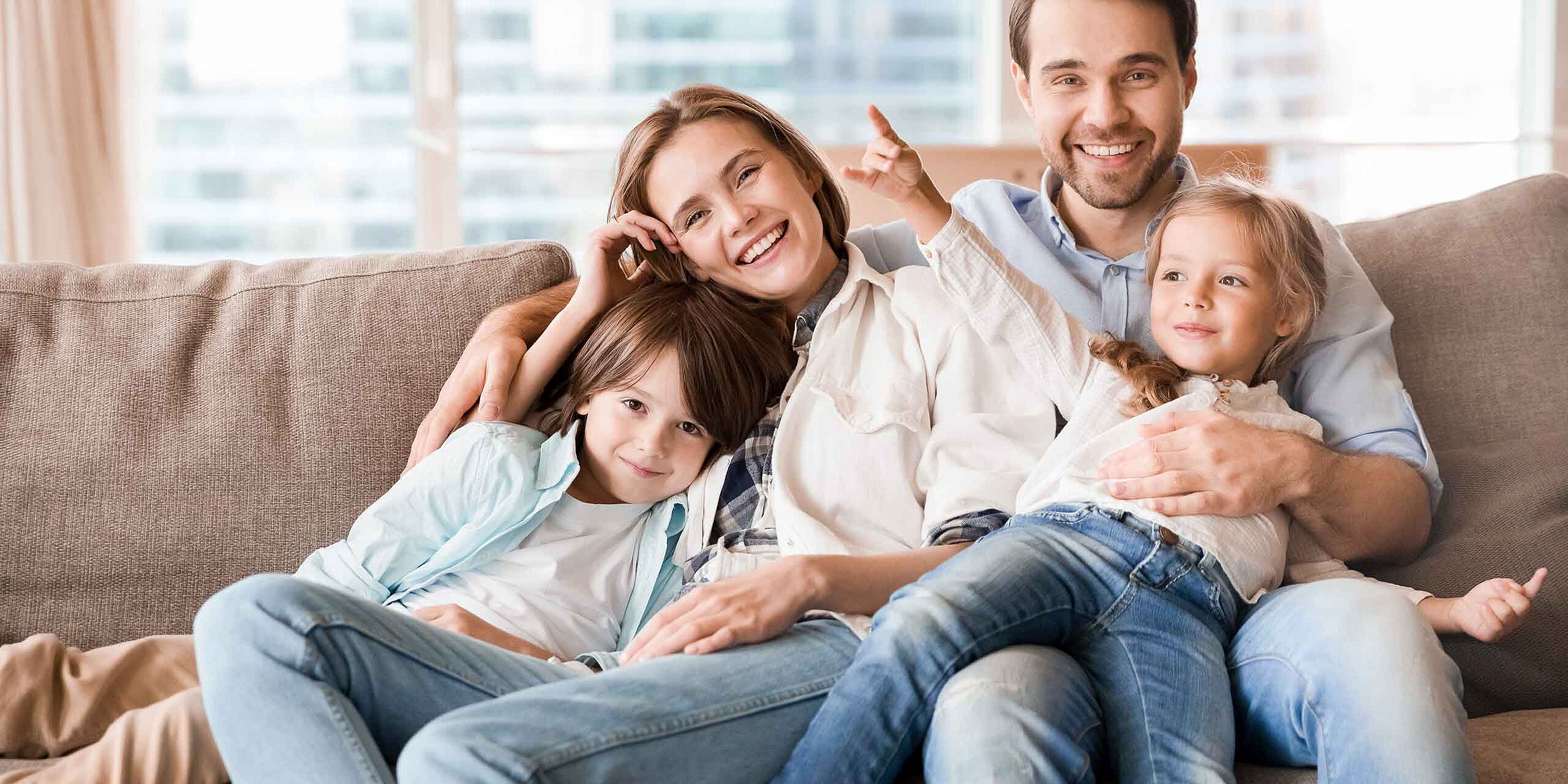 Glückliche Familie mit zwei kleinen Kindern sitzt gemeinsam auf dem Sofa