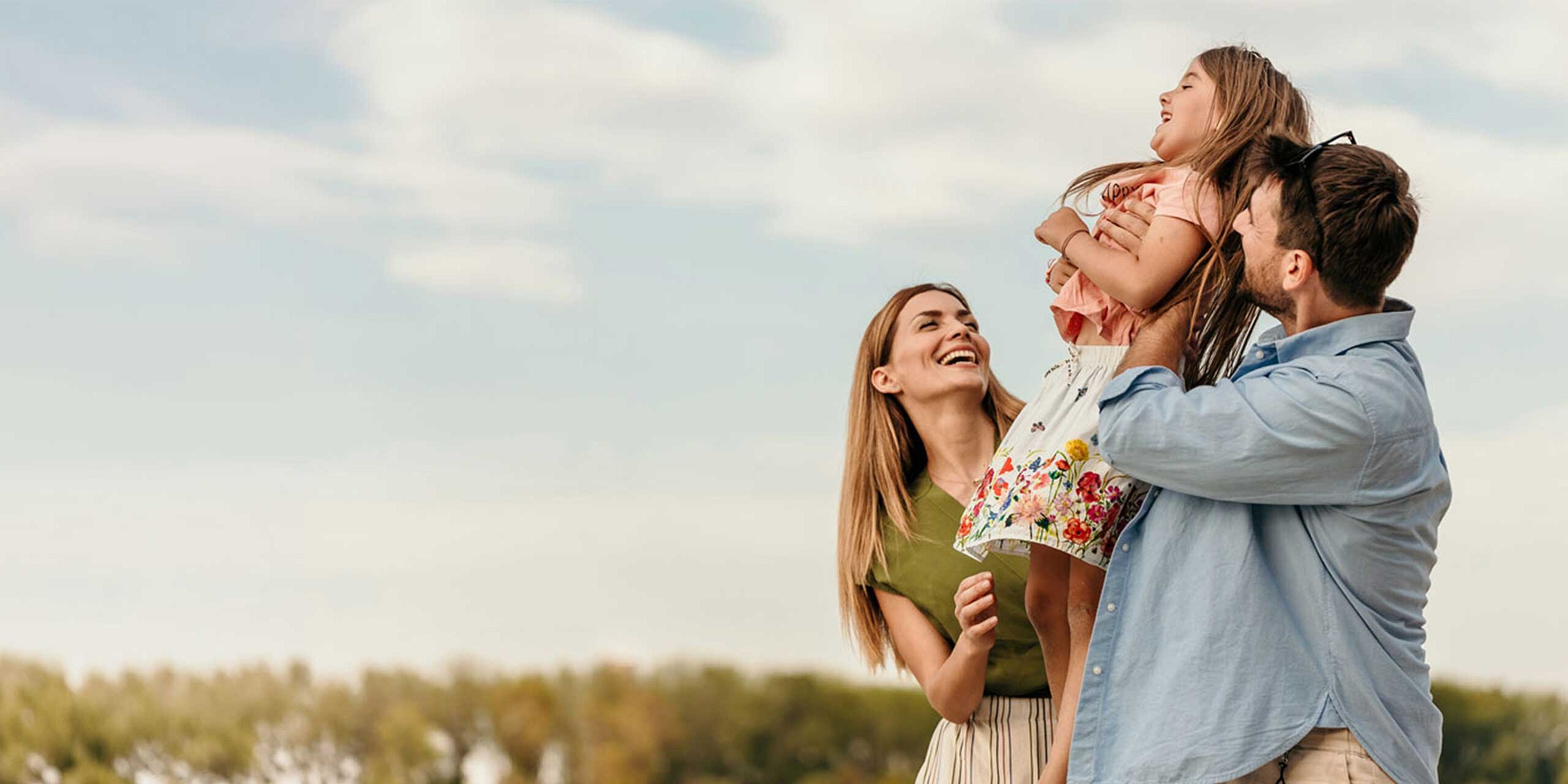 Ein Vater hebt seine lachende Tochter hoch, während die Mutter daneben lächelt.
