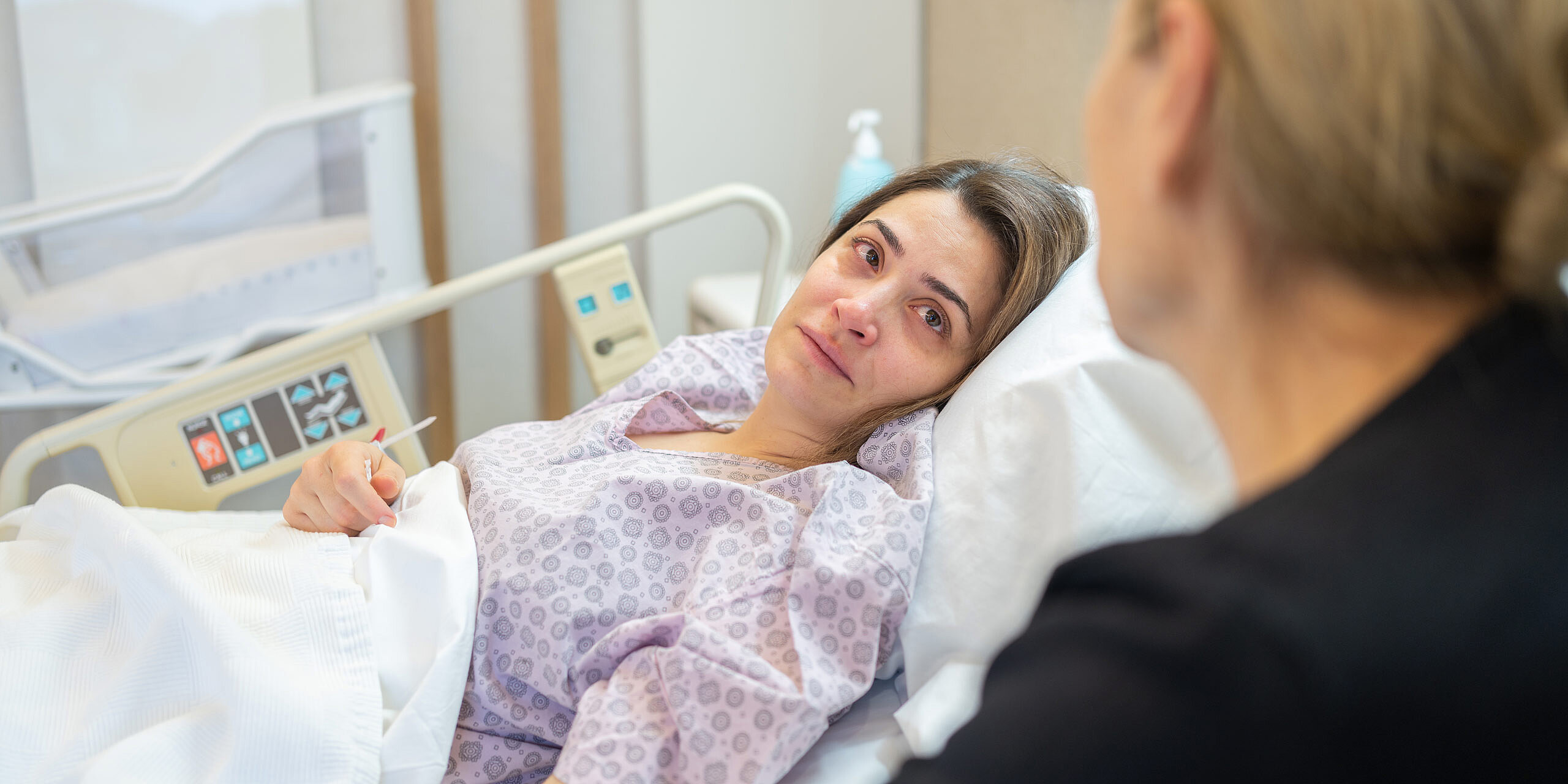 Frau liegt erschöpft im Krankenhausbett und wird betreut