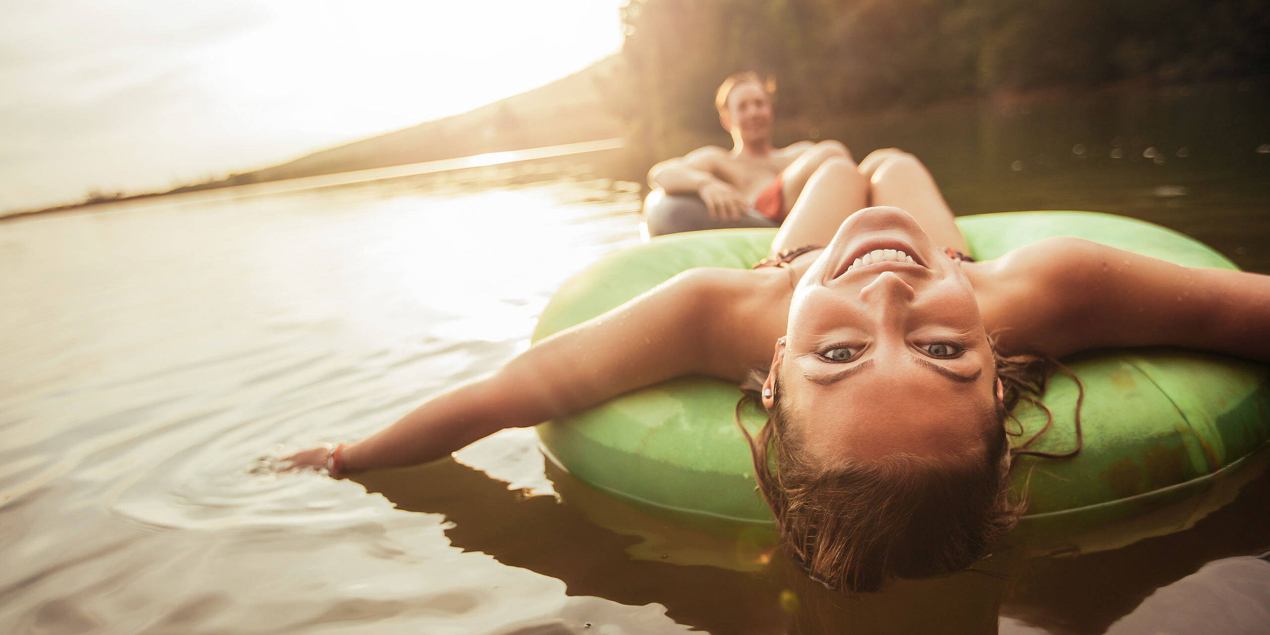 Pärchen auf großen Schwimmringen im Wasser, sie schaut nach hinten gelehnt in die Kamera