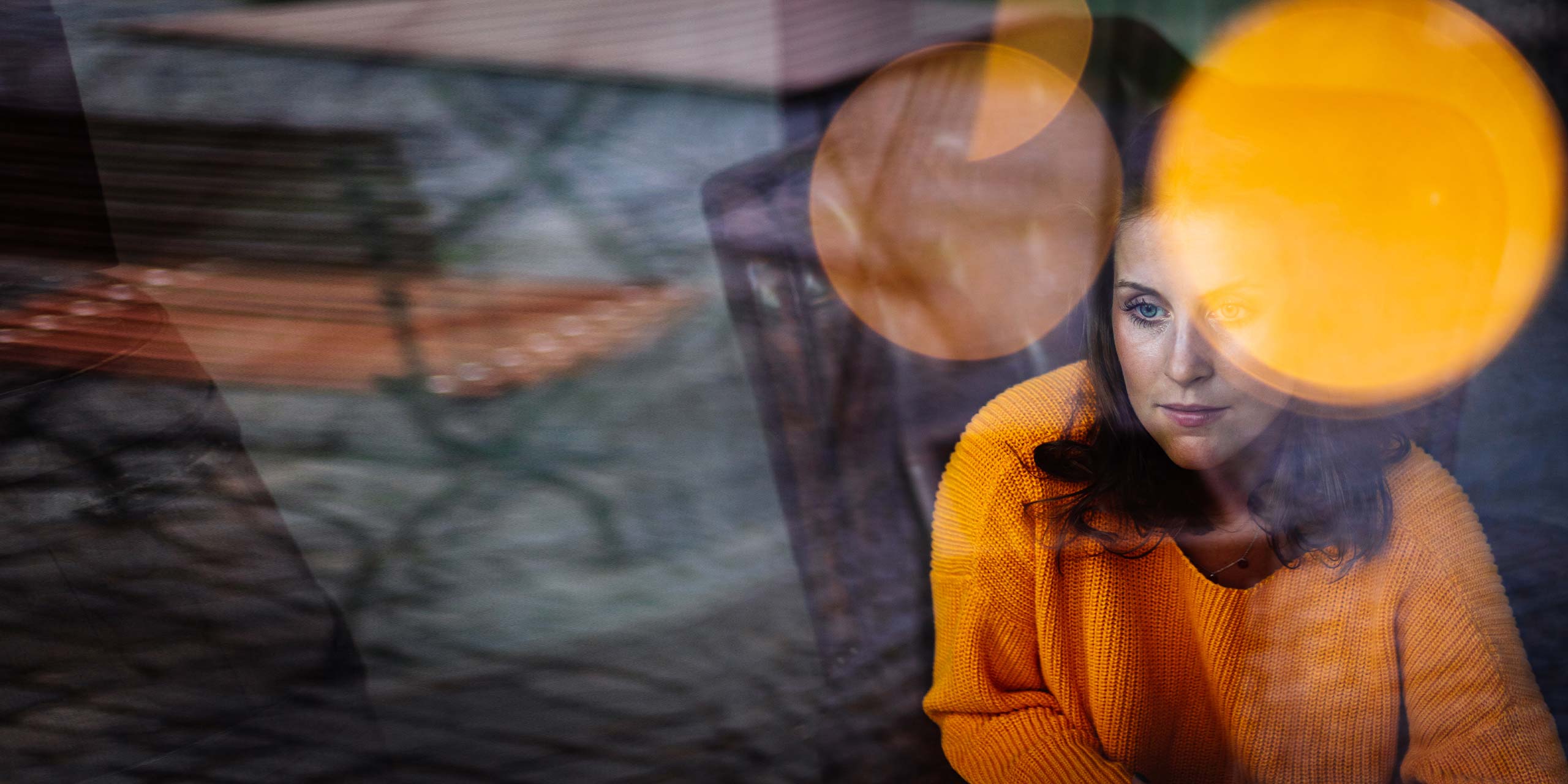 Traurig aussehende Frau sitzt hinter einer Glasscheibe mit Lichtpunkten