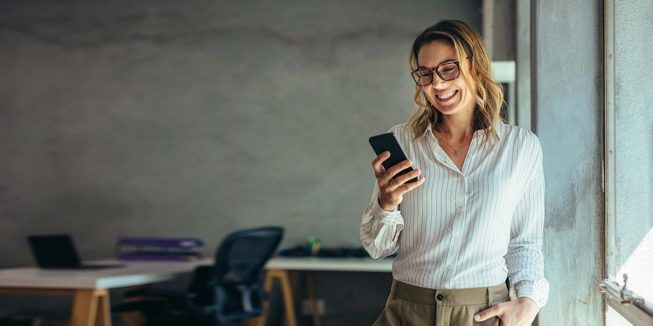 Frau in einem Büro schaut lächelnd auf Smartphone