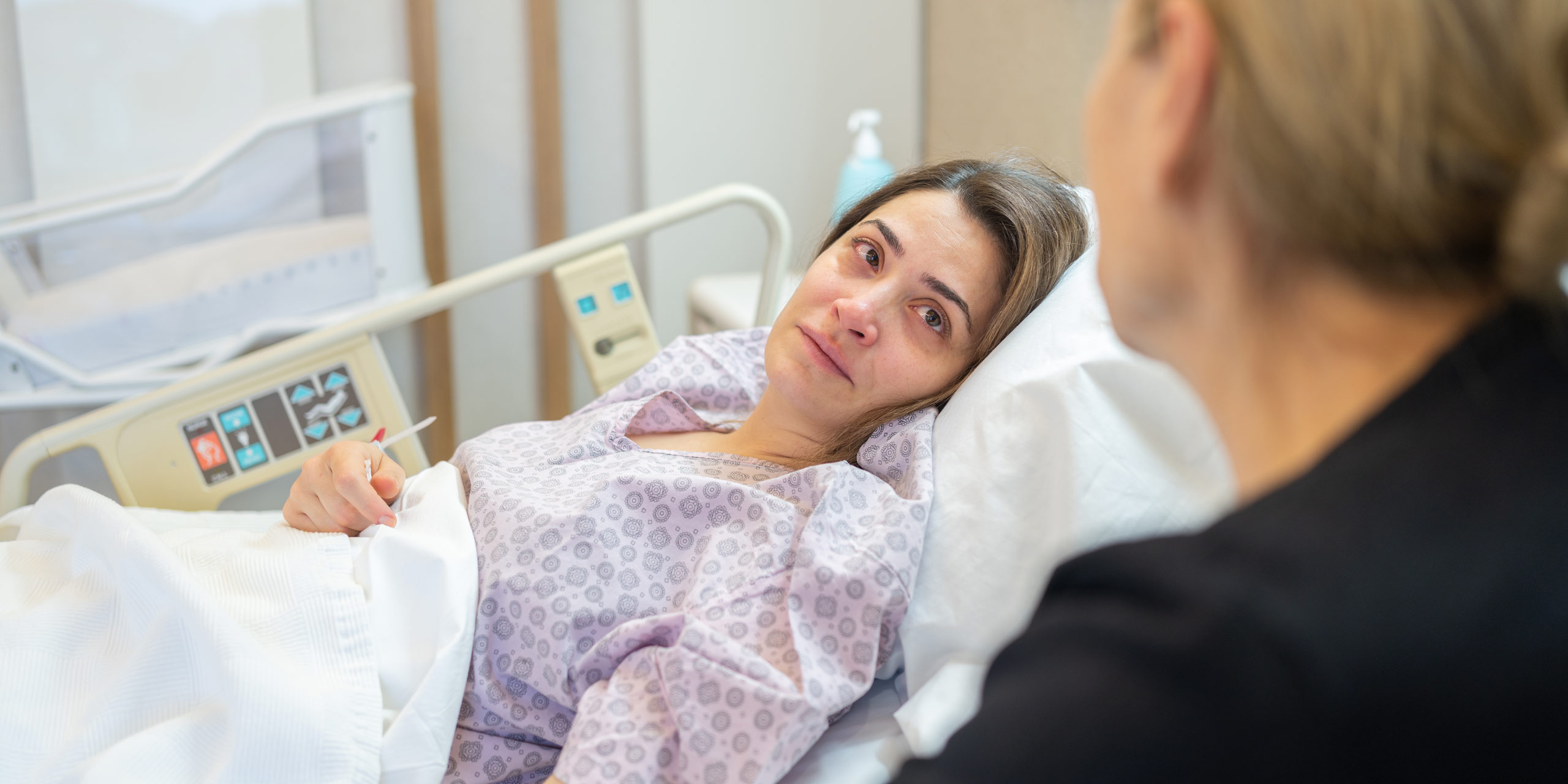 Frau liegt erschöpft im Krankenhausbett und wird betreut