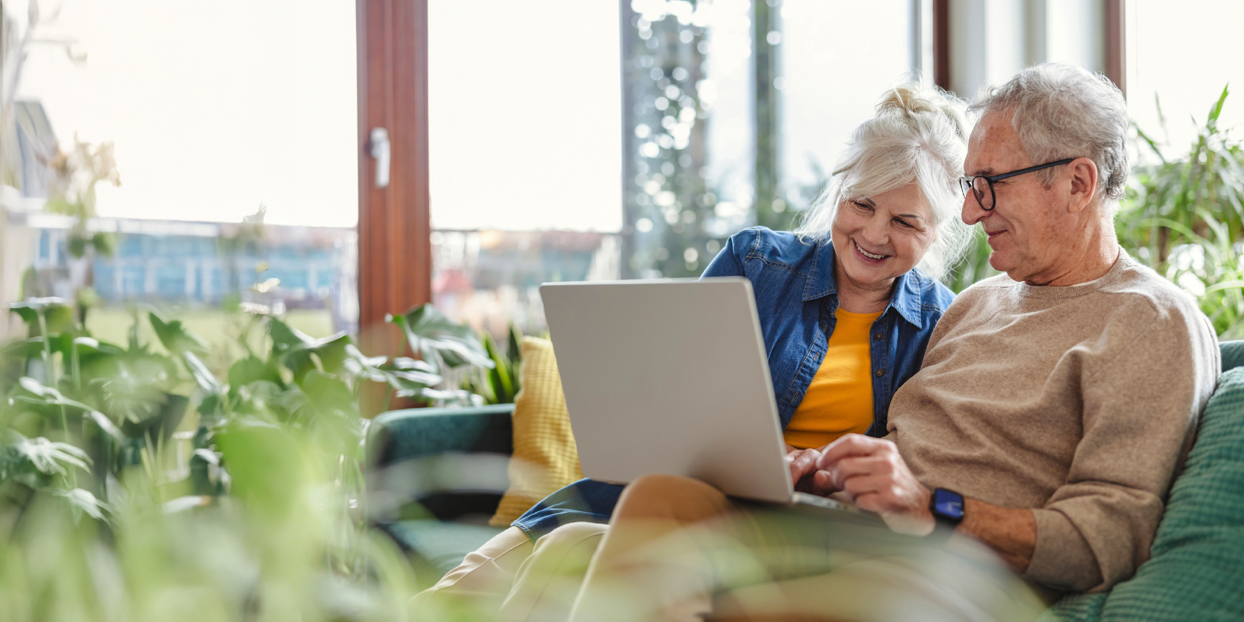 Älteres Paar sitzt zuhause und nutzt gemeinsam einen Laptop.