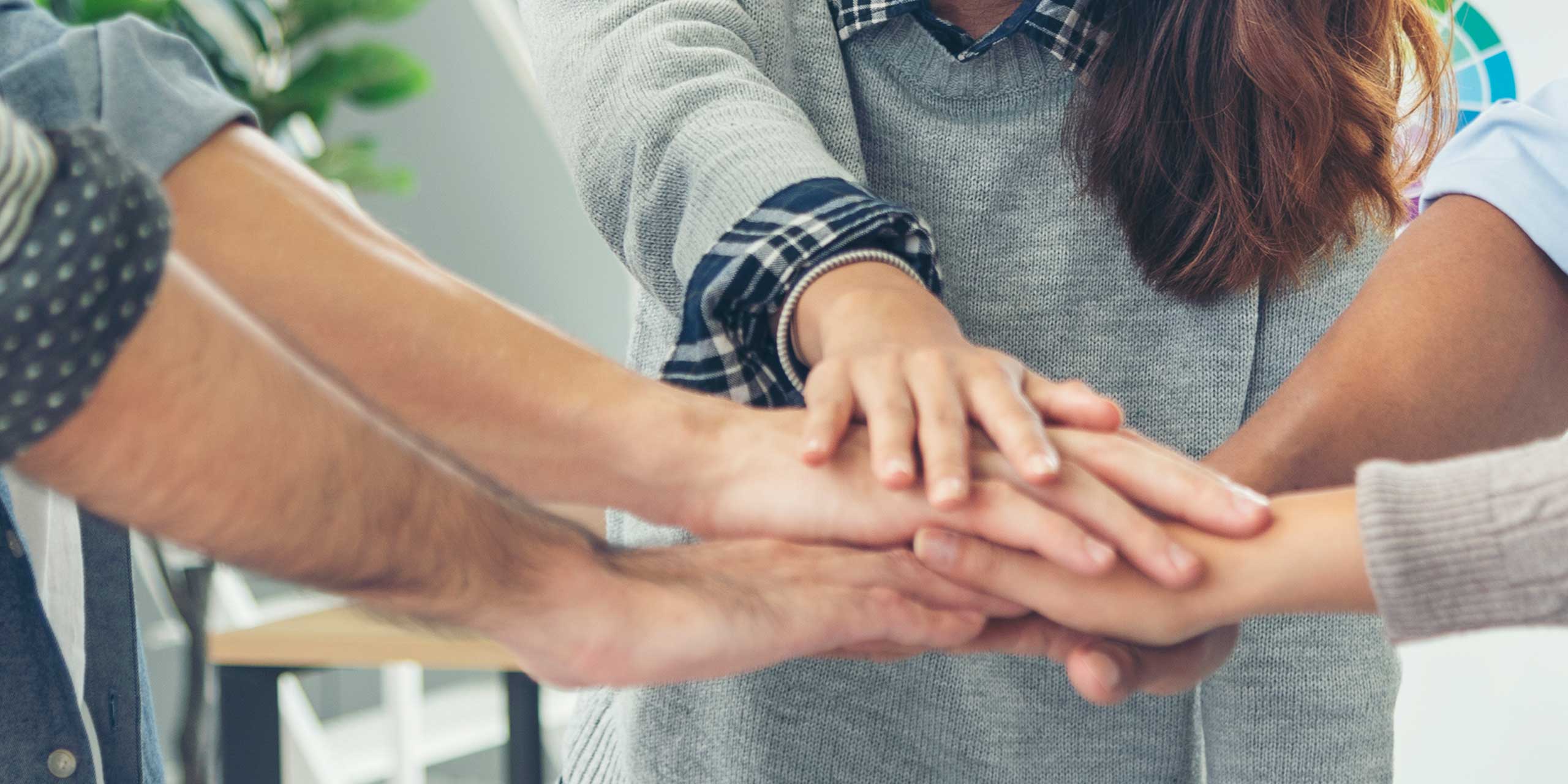 Gruppe von Menschen stapelt Hände übereinander, symbolisiert Zusammenarbeit und Zusammenhalt.