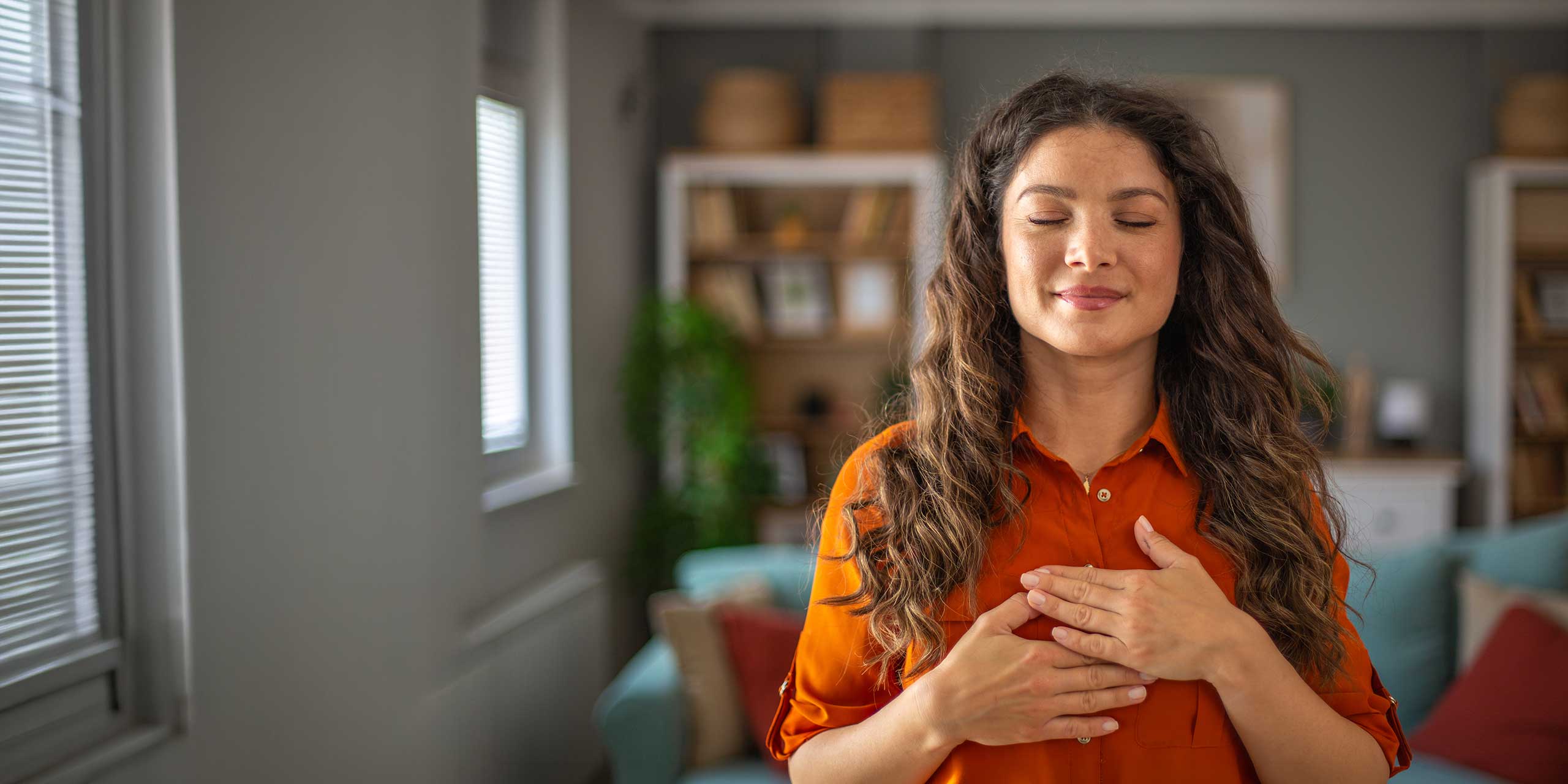 Frau mit geschlossenen Augen legt die Hände auf die Brust und konzentriert sich auf ihre Atmung in ruhiger Umgebung.