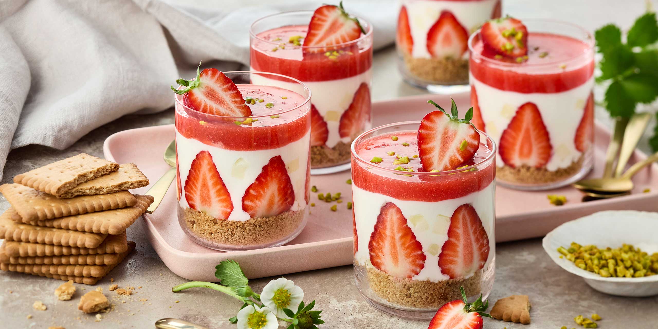 Mehrere Gläser mit Erdbeer-Dessert, geschichtet aus Keksboden, Creme und Erdbeerpüree, dekoriert mit frischen Erdbeeren.